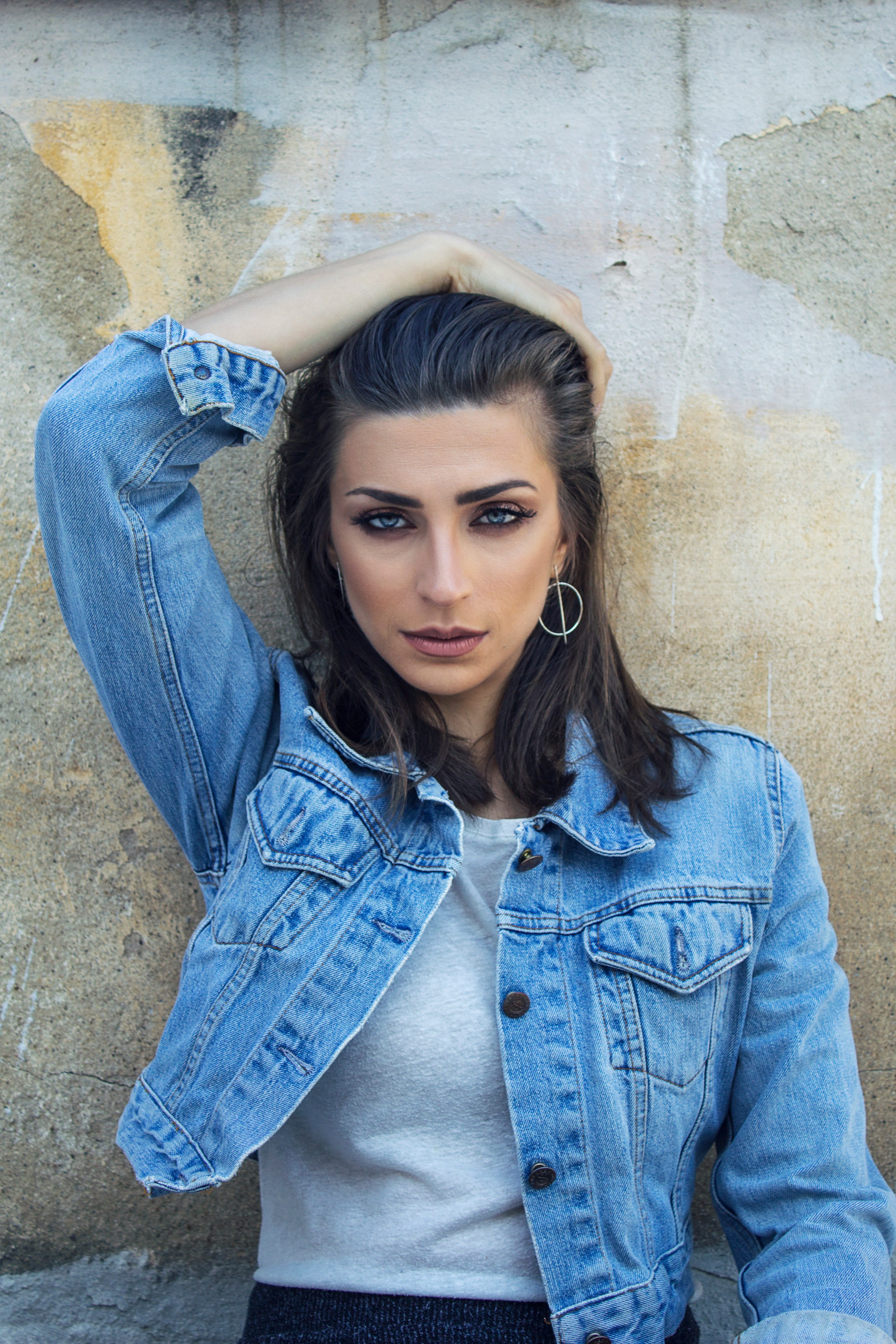 woman in blue denim button up jacket leaning on brown wall